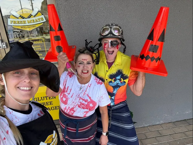 Three of the team in Halloween costume outside the shop holding jack-o-lantern traffic cones