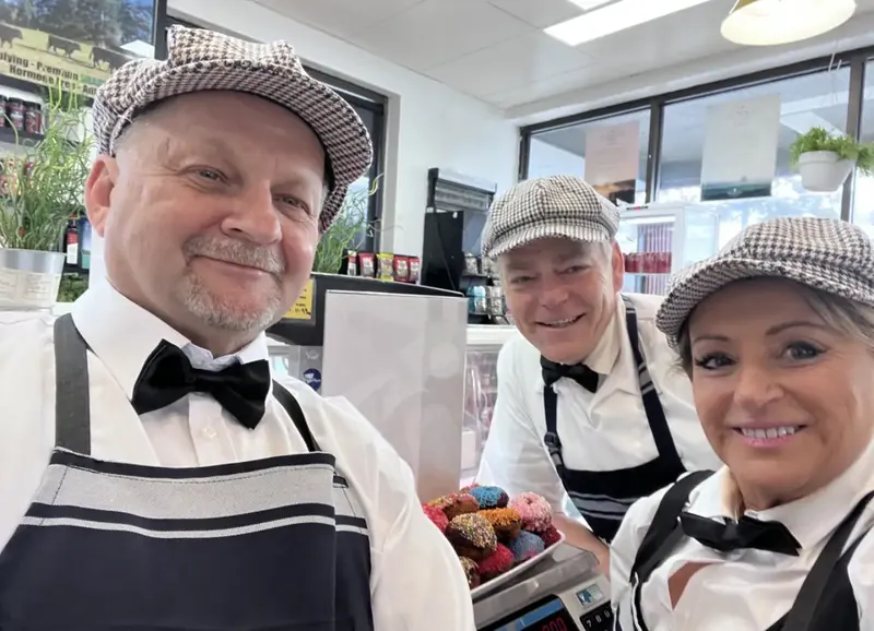 Three of the team in flat caps and bow ties holding a tray of iced doughnuts